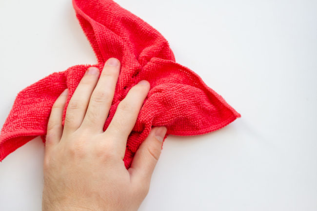 hand with red microfiber cloth on a white background. House cleaning Red microfibre cloth