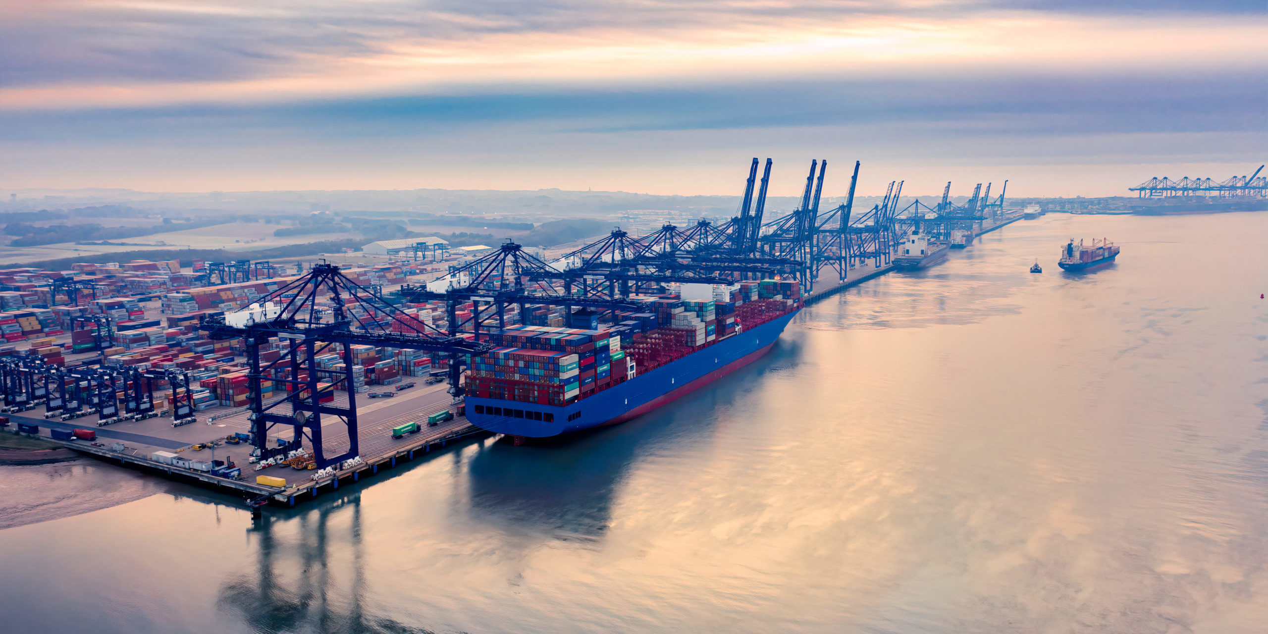 : Felixstowe Port, owned by Hutchinson Ports, is UK’s busiest container port and one of the largest in EuropeSunrise over Felixstowe Container Port a large container ship on the harbour wall being loaded with containers as a smaller ship in the background makes its way out to sea with a tug. : Felixstowe Port, owned by Hutchinson Ports, is UK’s busiest container port and one of the largest in Europe