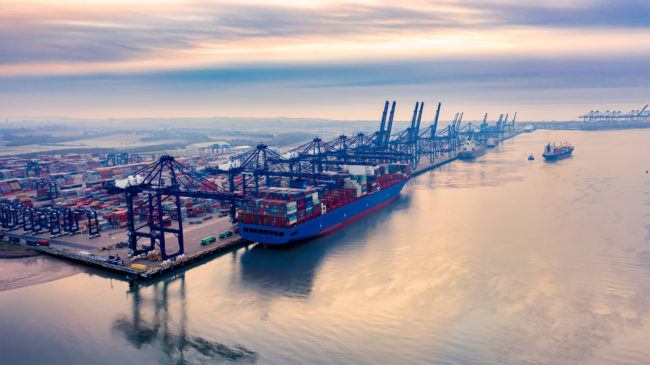 : Felixstowe Port, owned by Hutchinson Ports, is UK’s busiest container port and one of the largest in EuropeSunrise over Felixstowe Container Port a large container ship on the harbour wall being loaded with containers as a smaller ship in the background makes its way out to sea with a tug. : Felixstowe Port, owned by Hutchinson Ports, is UK’s busiest container port and one of the largest in Europe